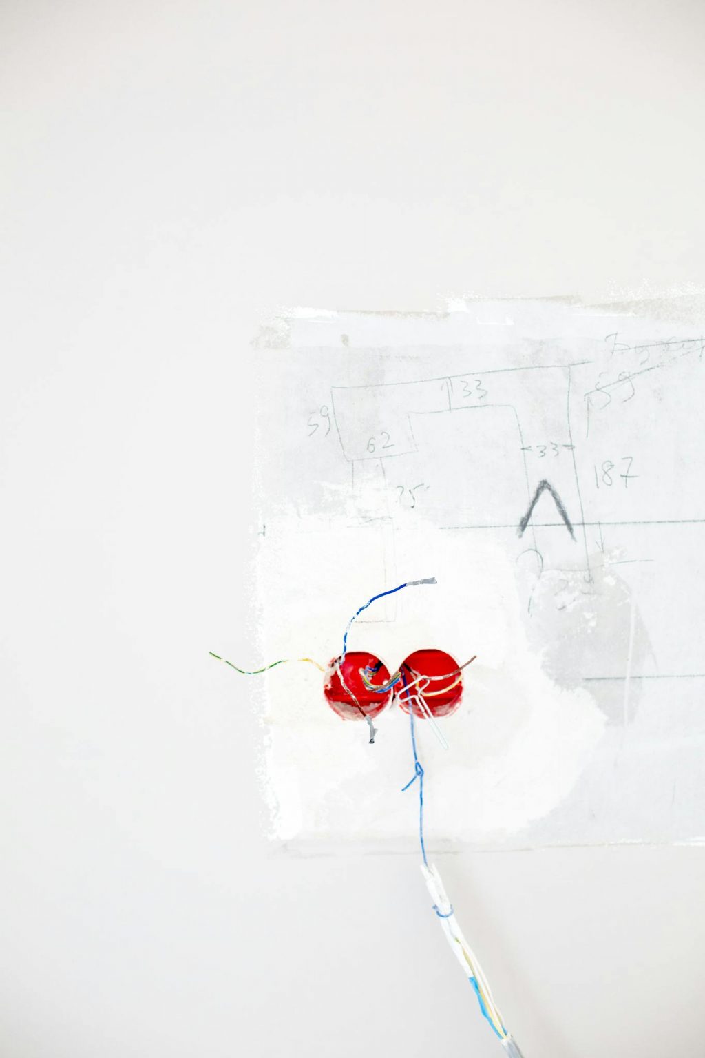 Minimalist photo of red electrical wiring emerging from a white wall background.